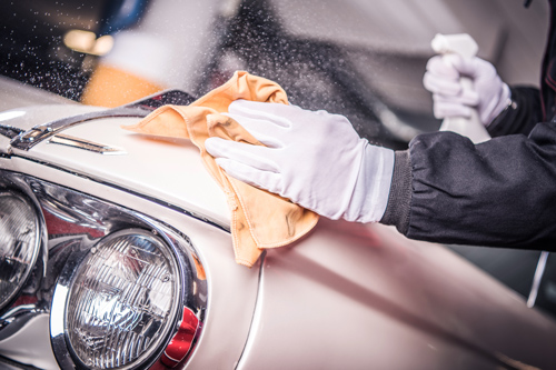 person cleaning car hood with cloth and spray in garage professional car care detailing service