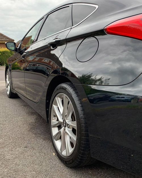 black car parked on the street with smooth tires and gleaming body reflecting the environment showcasing two doors and modern design