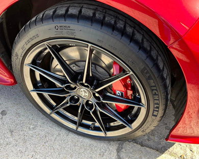 close up of a car wheel featuring black alloy rims and high performance tire with red brake caliper showing ideal for 5 spoke designs and five star ratings